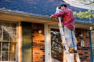 Person cleaning gutter from ladder on house